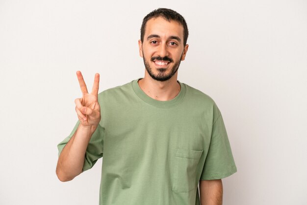 Young caucasian man isolated on white background showing victory sign and smiling broadly.