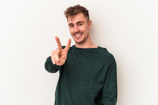 Young caucasian man isolated on white background showing victory sign and smiling broadly.