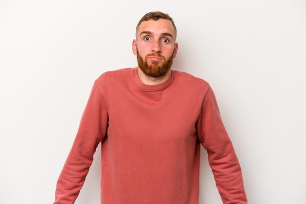 Young caucasian man isolated on white background shrugs shoulders and open eyes confused