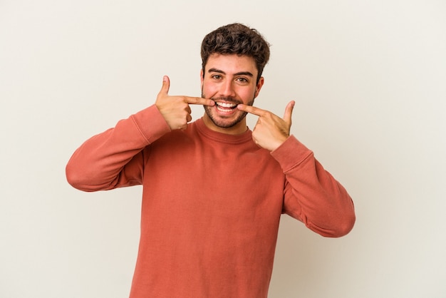 Young caucasian man isolated on white background smiles, pointing fingers at mouth.