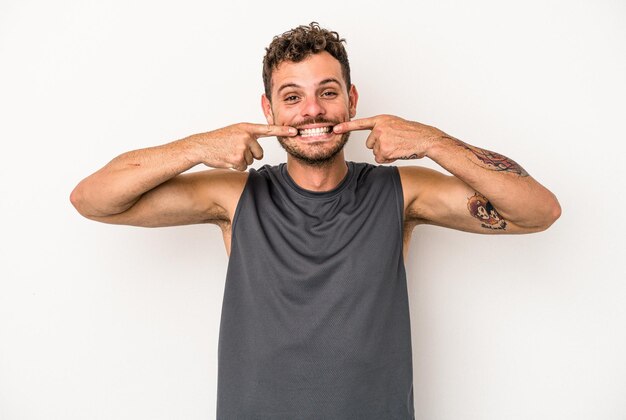 Young caucasian man isolated on white background smiles, pointing fingers at mouth.