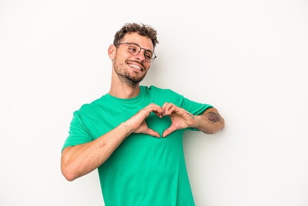 Giovane uomo caucasico isolato su sfondo bianco sorridente e mostrando una forma di cuore con le mani.