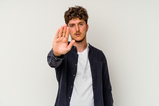 Young caucasian man isolated on white background standing with outstretched hand showing stop sign, preventing you.