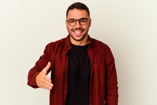 Foto giovane uomo caucasico isolato su sfondo bianco che allunga la mano alla macchina fotografica nel gesto di saluto.