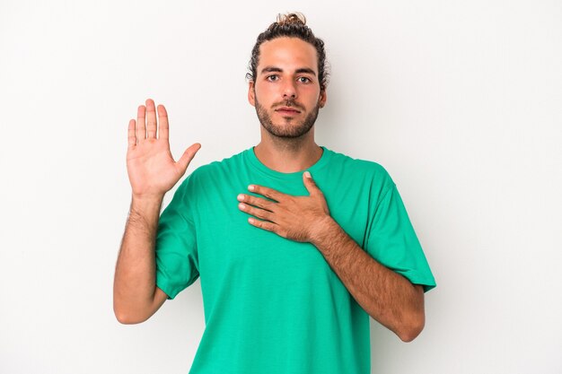 Young caucasian man isolated on white background taking an oath, putting hand on chest.
