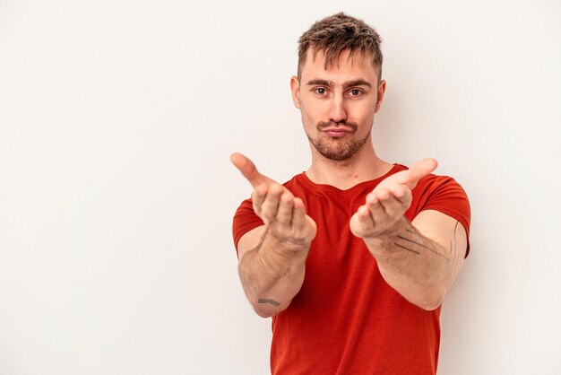 白い背景で隔離の若い白人男性は目をまばたきし、手で大丈夫なジェスチャーを保持します。