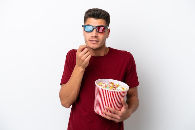 Young caucasian man isolated on white background with 3d glasses and holding a big bucket of popcorns