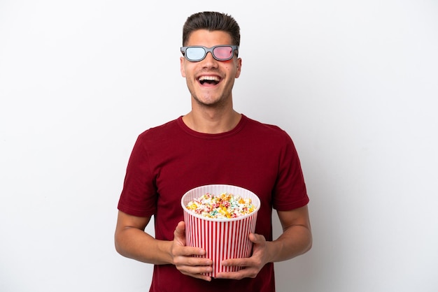 Молодой кавказский мужчина изолирован на белом фоне в 3d-очках и держит большое ведро попкорна