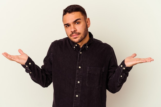 Young caucasian man isolated on white confused and doubtful shrugging shoulders to hold a copy space.