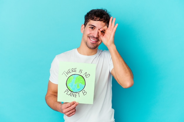 Young caucasian man isolated on white excited keeping ok gesture on eye.