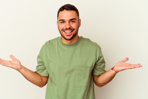 Young caucasian man isolated on white makes scale with arms, feels happy and confident.