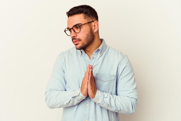 Young caucasian man isolated on white praying, showing devotion, religious person looking for divine inspiration.