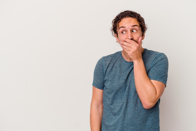 Young caucasian man isolated on white thoughtful looking to a copy space covering mouth with hand.