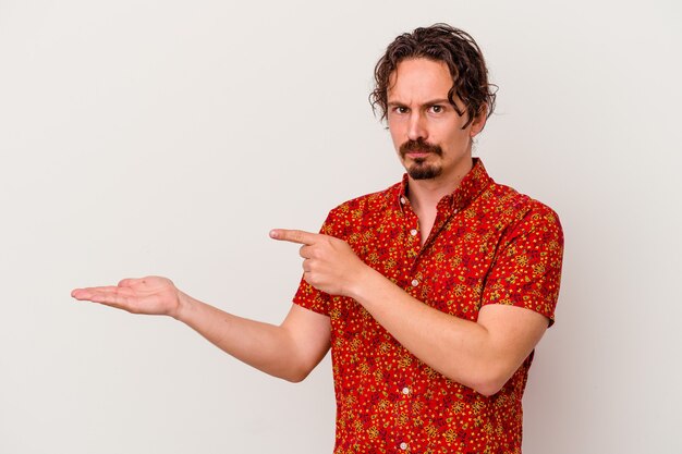 Young caucasian man isolated on white wall excited holding a copy space on palm.