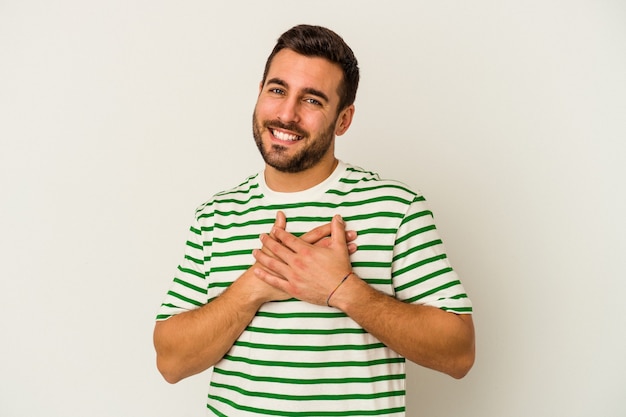 Young caucasian man isolated on white wall has friendly expression, pressing palm to chest