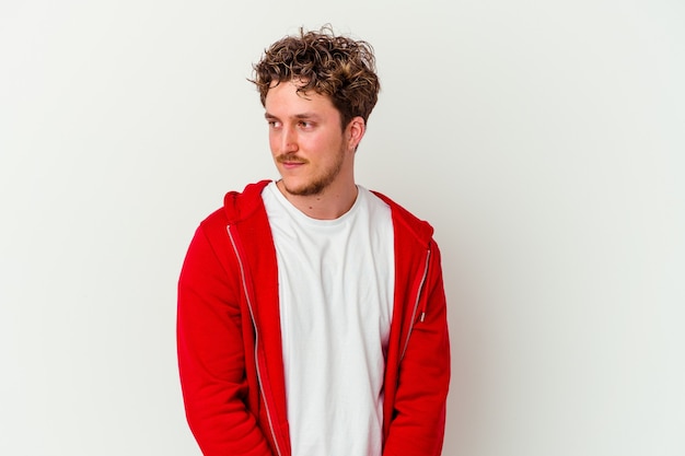 Young caucasian man isolated on white wall looks aside smiling, cheerful and pleasant.