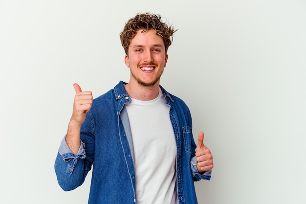 Young caucasian man isolated on white wall raising both thumbs up, smiling and confident.