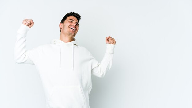 Young caucasian man isolated on white wall raising fist after a victory, winner concept.