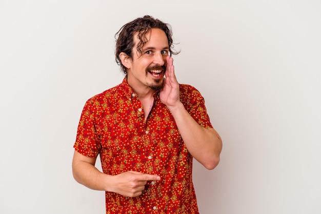 Young caucasian man isolated on white wall saying a gossip, pointing to side reporting something