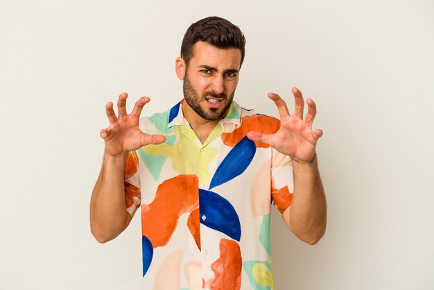 Young caucasian man isolated on white wall showing claws imitating a cat, aggressive gesture.