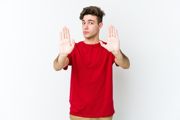 Young caucasian man isolated on white wall standing with outstretched hand showing stop sign, preventing you.