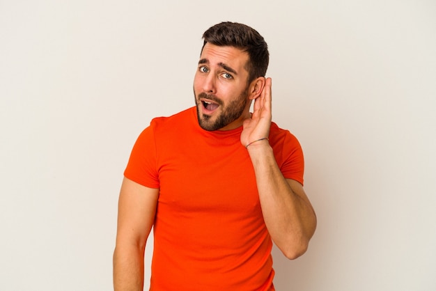 Young caucasian man isolated on white wall trying to listening a gossip