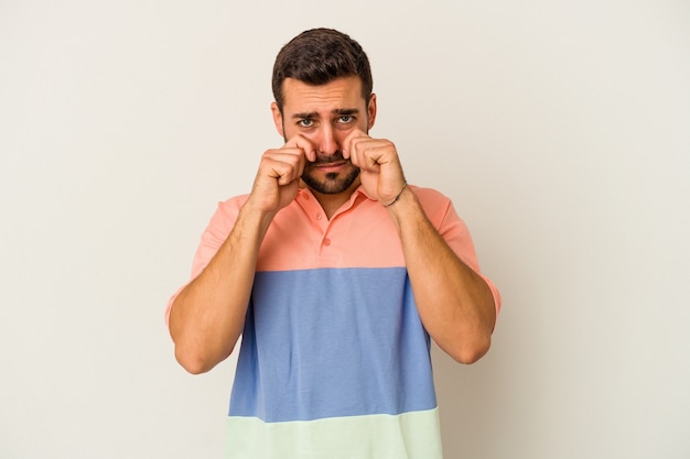 Young caucasian man isolated on white wall whining and crying disconsolately.