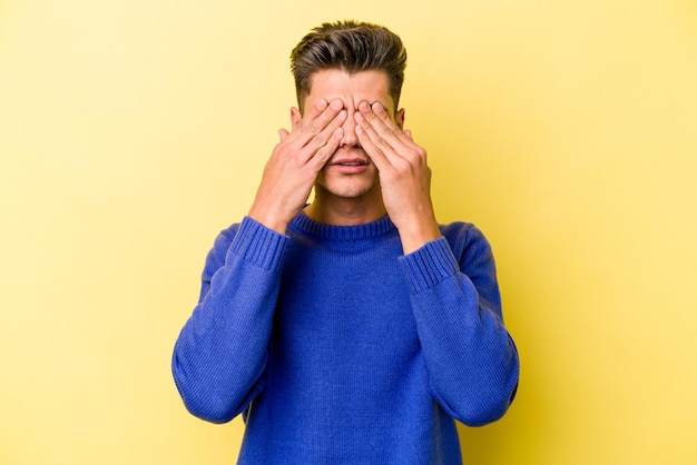 Young caucasian man isolated on yellow background afraid covering eyes with hands.