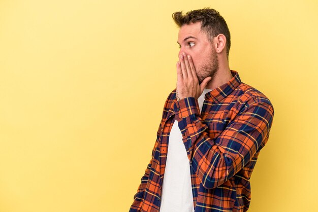 Young caucasian man isolated on yellow background being shocked because of something she has seen.