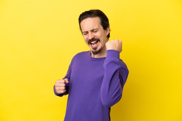 Young caucasian man isolated on yellow background celebrating a victory