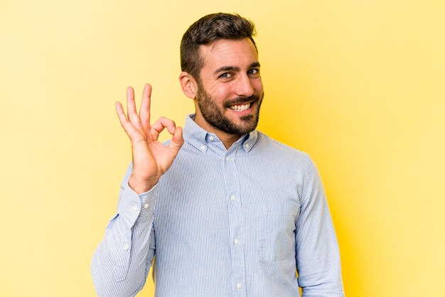 Young caucasian man isolated on yellow background cheerful and confident showing ok gesture