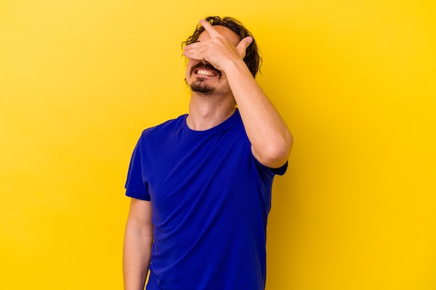 Young caucasian man isolated on yellow background covers eyes with hands, smiles broadly waiting for a surprise.