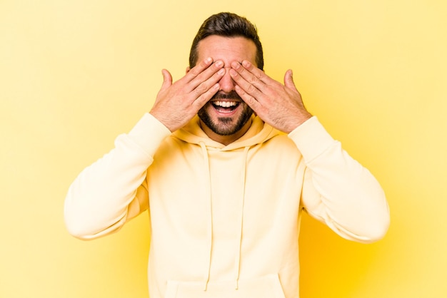 Young caucasian man isolated on yellow background covers eyes with hands smiles broadly waiting for a surprise