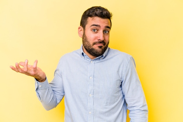 Young caucasian man isolated on yellow background doubting and shrugging shoulders in questioning gesture