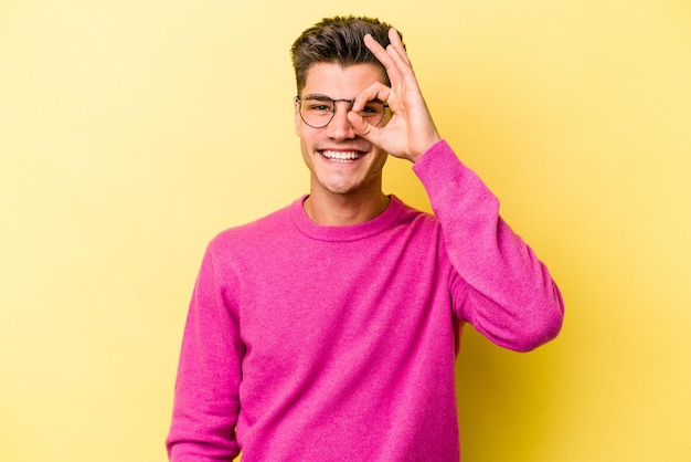 Young caucasian man isolated on yellow background excited keeping ok gesture on eye.