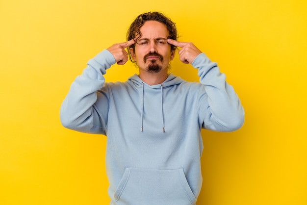 Young caucasian man isolated on yellow background focused on a task, keeping forefingers pointing head.