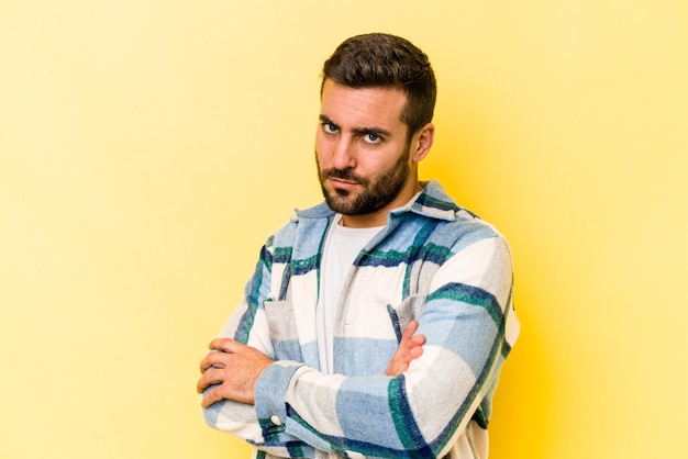 Young caucasian man isolated on yellow background frowning face in displeasure keeps arms folded