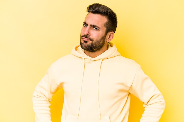 Young caucasian man isolated on yellow background frowning face in displeasure keeps arms folded