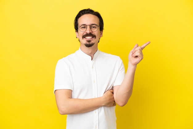 Young caucasian man isolated on yellow background happy and pointing up