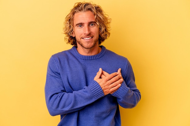 Young caucasian man isolated on yellow background has friendly expression, pressing palm to chest. Love concept.