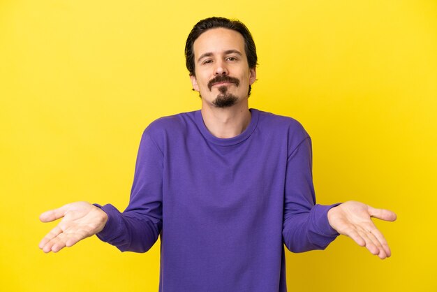Young caucasian man isolated on yellow background having doubts
