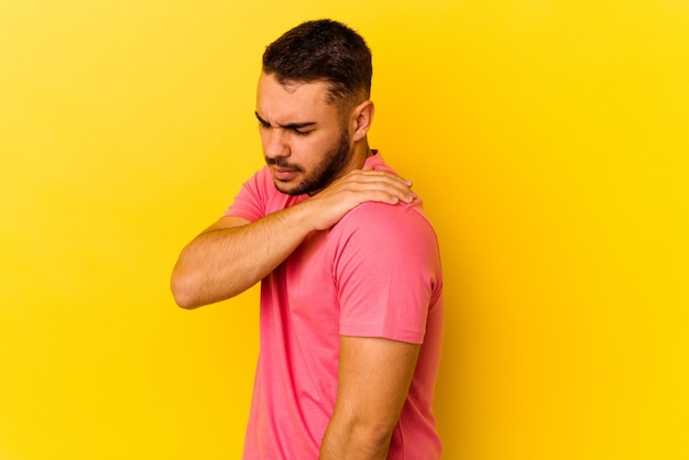 Giovane uomo caucasico isolato su sfondo giallo che ha un dolore alla spalla.
