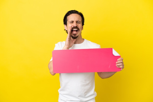 Young caucasian man isolated on yellow background holding an empty placard and shouting