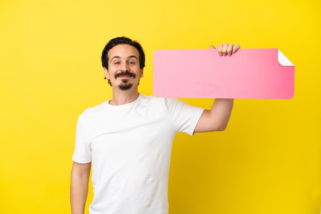 Young caucasian man isolated on yellow background holding an empty placard