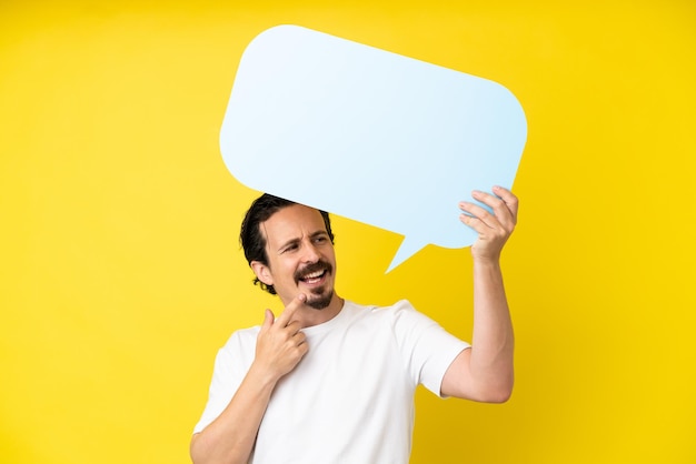 Young caucasian man isolated on yellow background holding an empty speech bubble and pointing it