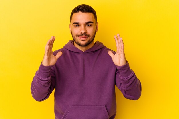 Young caucasian man isolated on yellow background holding something little with forefingers, smiling and confident.