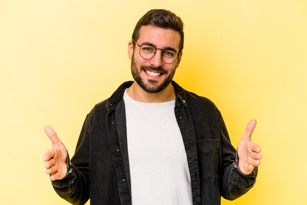 Young caucasian man isolated on yellow background holding something with both hands product presentation