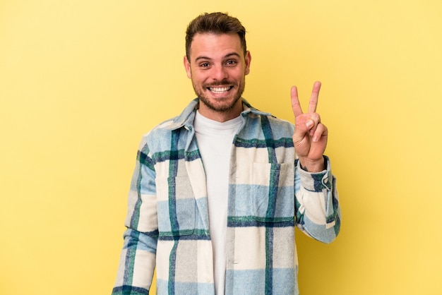 Young caucasian man isolated on yellow background joyful and carefree showing a peace symbol with fingers