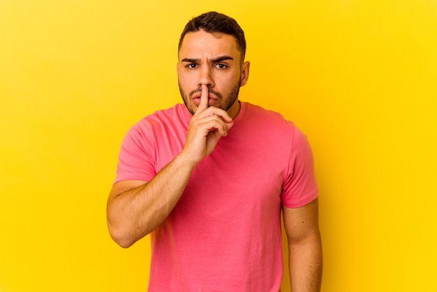 Young caucasian man isolated on yellow background keeping a secret or asking for silence.
