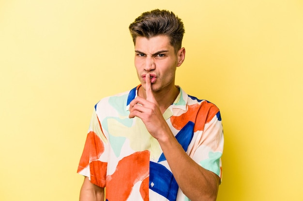 Young caucasian man isolated on yellow background keeping a secret or asking for silence.